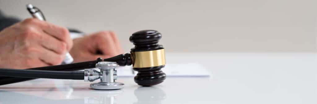 Lawyer Signing A Legal Document With A Gavel And Stethoscope On The Desk, Representing Medical Malpractice Law