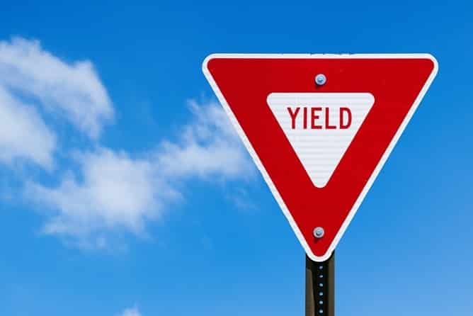 Leyes De Derecho De Paso Y Falta De Ceder El Paso En Nevada 1 A Close-Up Shot Of A Standard Triangular Yield Sign Against A Bright Blue Sky With Light Clouds. The Sign Has A Thick Red Outer Border And A White Inverted Triangle In The Center Containing The Word &Quot;Yield&Quot; In Red Capital Letters.