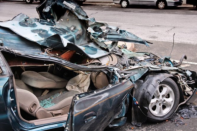 Primer Plano De Un Automóvil De Color Verde Oscuro Completamente Destrozado Tras Un Accidente De Tráfico, Con El Techo Aplastado, Las Bolsas De Aire Desplegadas Y Visibles Daños Estructurales Graves.