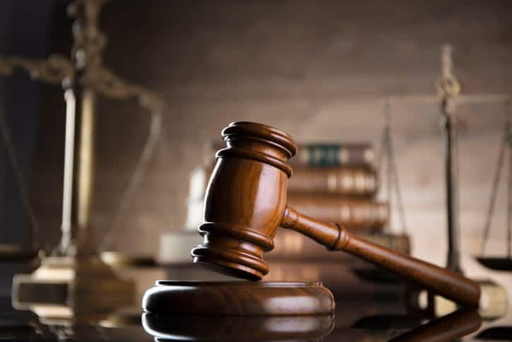 ¿Con Qué Frecuencia Los Acuerdos Por Accidentes De Auto Superan Los Límites De La Póliza? 2 Primer Plano De Un Mazo De Madera Sobre Su Base En Un Escritorio, Con Libros Jurídicos Y Una Balanza De La Justicia Difuminados En El Fondo.