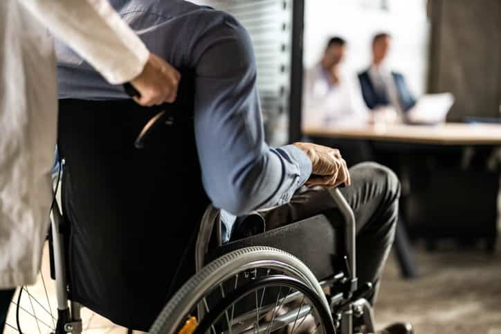 Lesión De La Médula Espinal En Summerlin 1 Vista Trasera De Un Hombre En Silla De Ruedas Siendo Asistido Mientras Se Dirige A Una Reunión Con Abogados En Una Oficina Profesional.